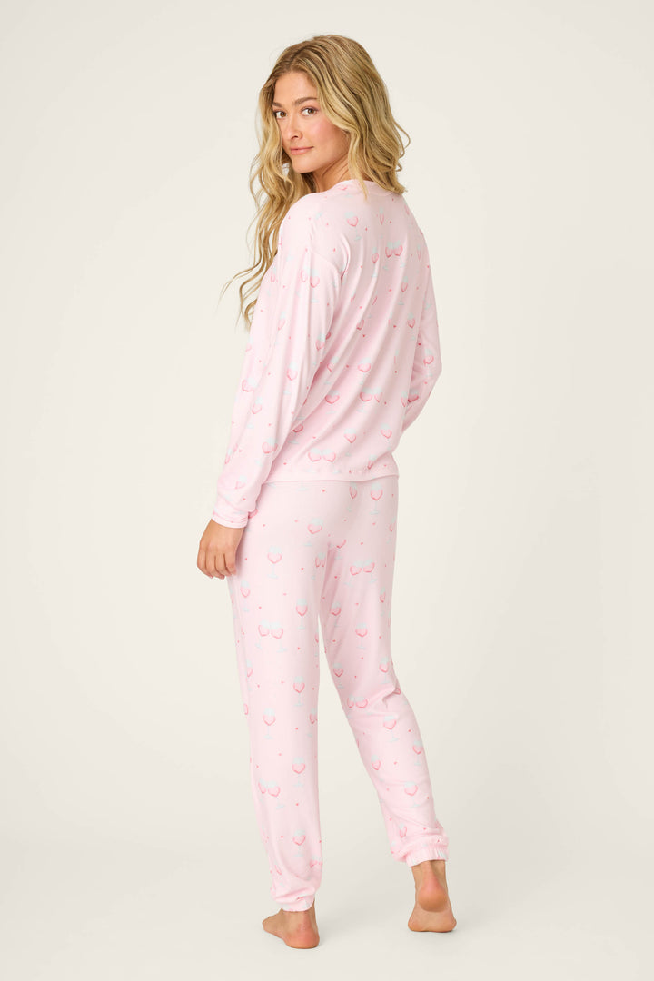 A person with long blonde hair stands barefoot, slightly turned, wearing the P.J. Salvage Happy Hour Wine Glass Print PJ Set against a plain light background.