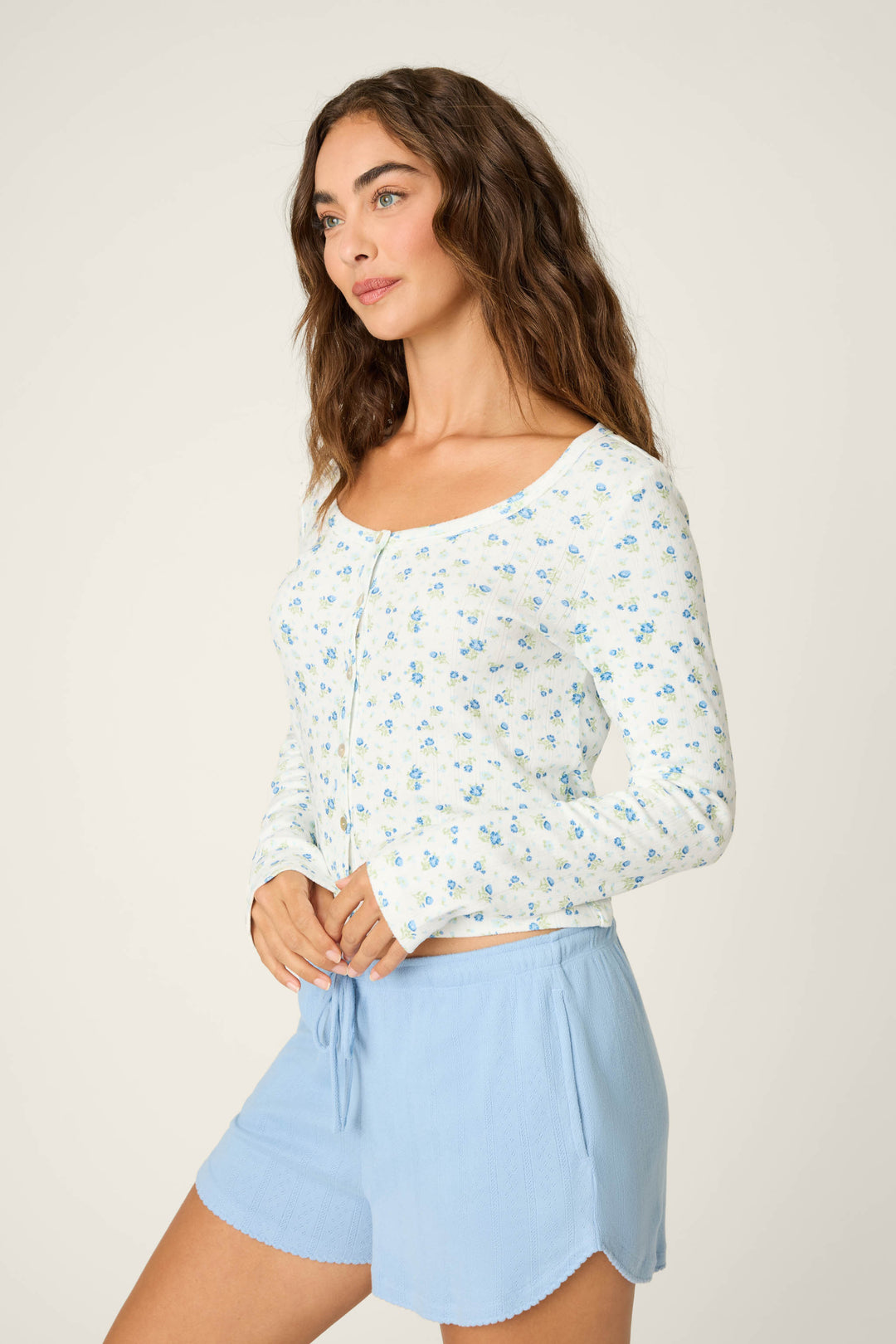 A person with long brown hair is wearing the More Amour Ditsy Floral Long Sleeve Pointelle Top by P.J. Salvage, styled with light blue drawstring shorts, standing against a plain light background.