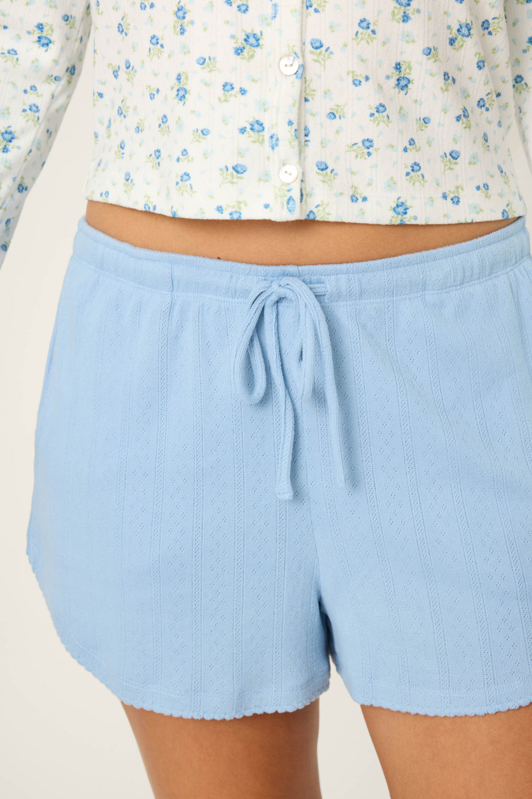 A person wears P.J. Salvage More Amour Blue Dream Pointelle Shorts and a white button-up shirt with blue and green floral print. The image is cropped from mid-torso to upper thigh.