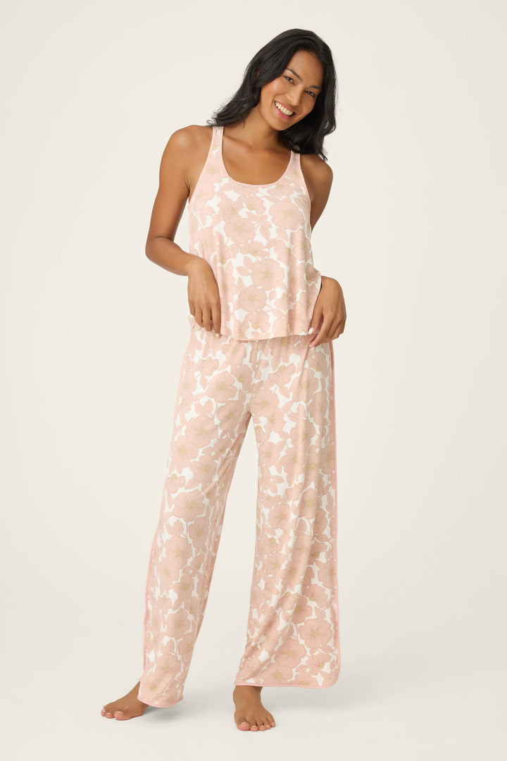 A woman stands barefoot against a plain background, smiling with one hand on her hip, wearing the P.J. Salvage Poppy Dreams Floral Tank Top and matching wide-leg pajama pants in pink and white.