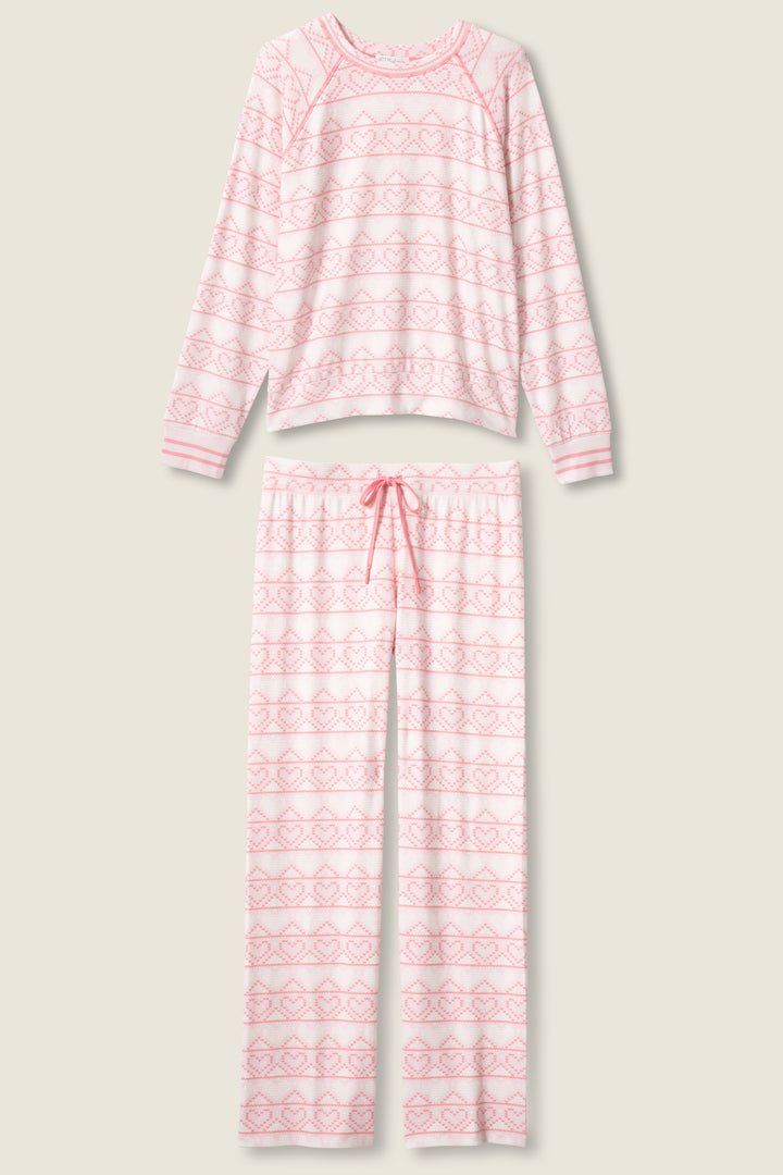 The P.J. Salvage Fairisle Heart Print Peachy PJ Set features a long-sleeve top and full-length pants in light pink and white with a heart pattern, plus an adjustable drawstring waist. The set is displayed flat on a neutral background.
