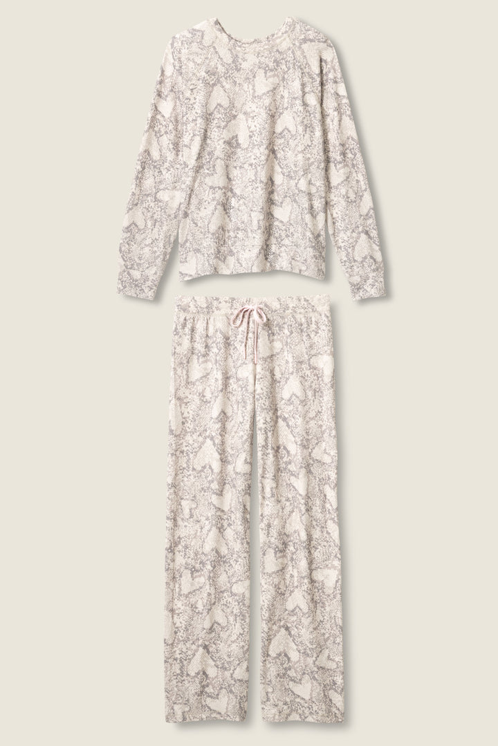 The P.J. Salvage Snakeskin Heart Print Peachy PJ Set includes a long-sleeve top and drawstring pants, both in a light cream base with gray and white snakeskin heart print, laid flat on a neutral background.