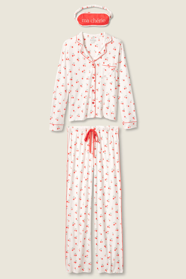 The P.J. Salvage Valentine's Day Cherry Print 3-Piece PJ Set features a white pajama set with red cherry print, a long-sleeve button-up top with red piping and pocket, long pants with red drawstring, and a "ma chérie" sleep mask.