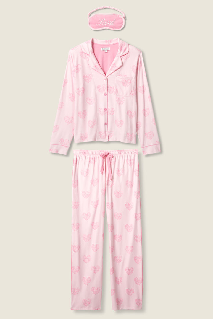 The P.J. Salvage Valentine's Day Leopard Hearts Print 3-Piece PJ Set is displayed with a pink sleep mask embroidered with "Lived" in cursive, shown above the matching long-sleeve pajama top and pants featuring a heart pattern.