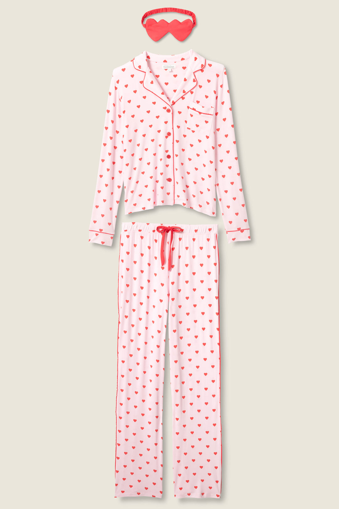 The P.J. Salvage Wildest Dreams Heart Print 3-Piece PJ Set features a pink long-sleeve button-up top, drawstring pants with red heart prints, and a matching sleep mask, displayed on a light beige background.