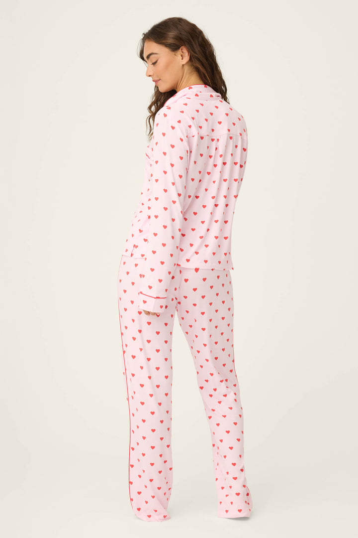 A person stands facing away, wearing the Wildest Dreams Heart Print 3-Piece PJ Set by P.J. Salvage, featuring a white base with a red heart pattern. The background is plain and neutral.