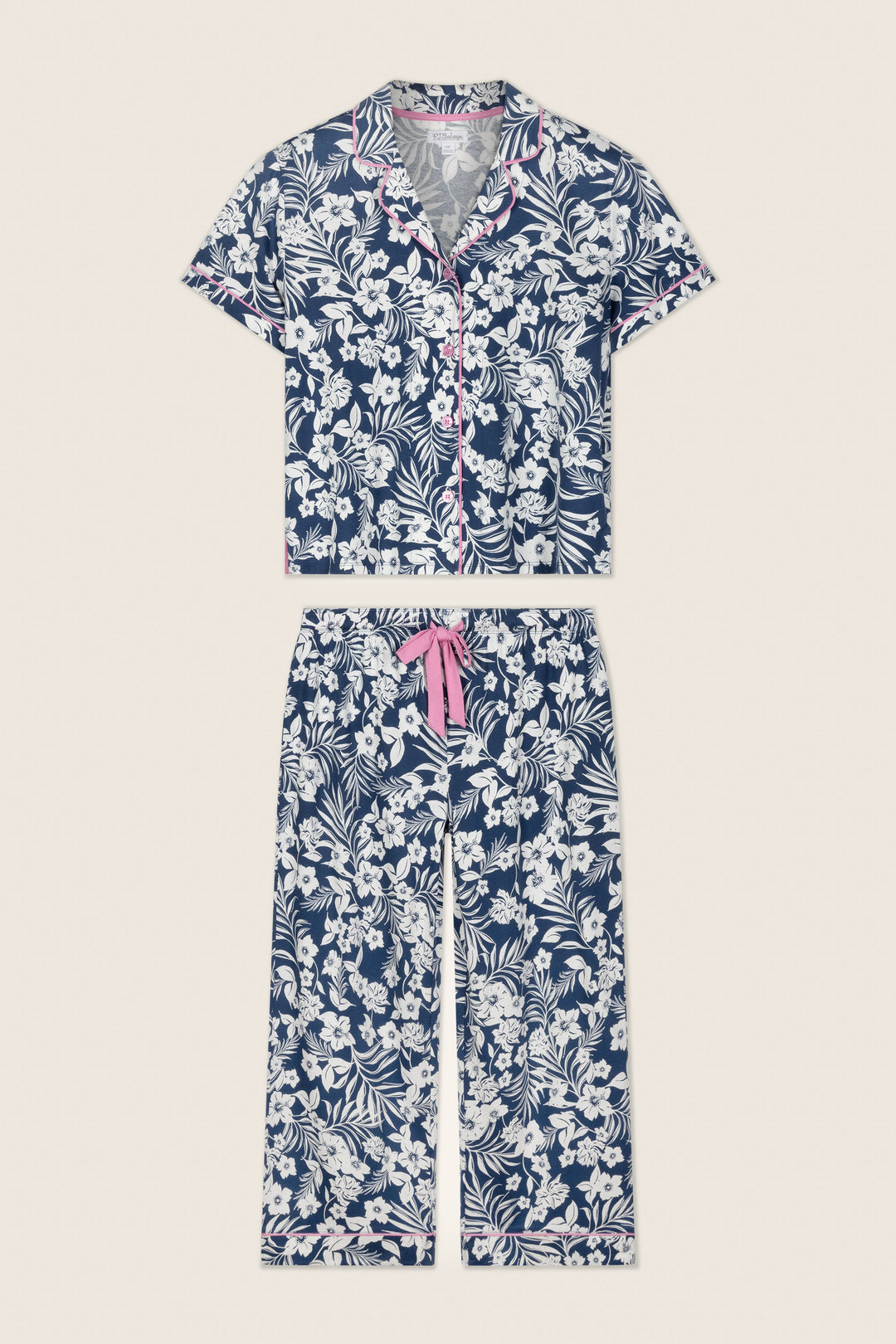 The P.J. Salvage Cotton Jersey Midnight Garden Cropped PJ Set features a navy and white floral short-sleeve button-up top, cropped pants with pink trim on the collar and cuffs, and a pink drawstring waist.