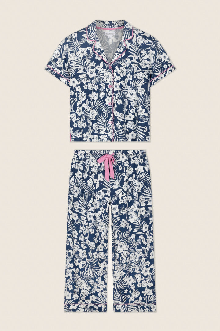 The P.J. Salvage Cotton Jersey Midnight Garden Cropped PJ Set features a navy and white floral short-sleeve button-up top, cropped pants with pink trim on the collar and cuffs, and a pink drawstring waist.