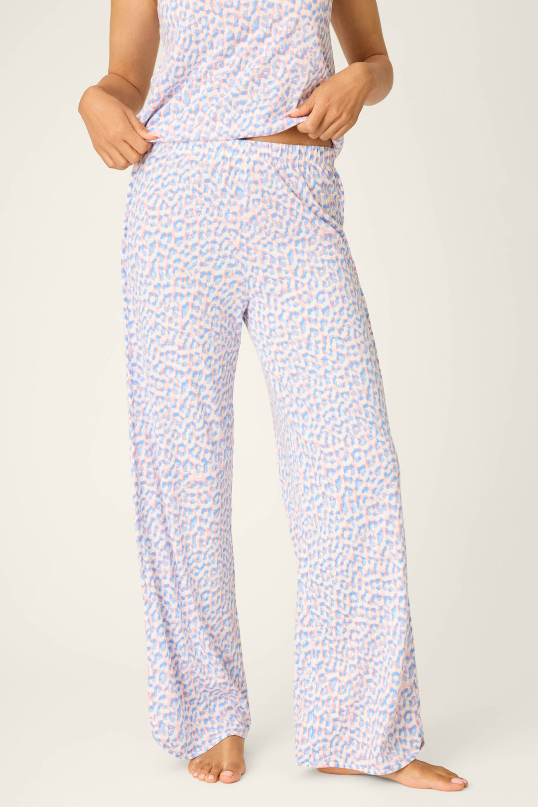 A person stands barefoot, adjusting the waistband of P.J. Salvage Animal Lover Leopard Print Open Leg Pants, shown from shoulders down with a matching pajama top.
