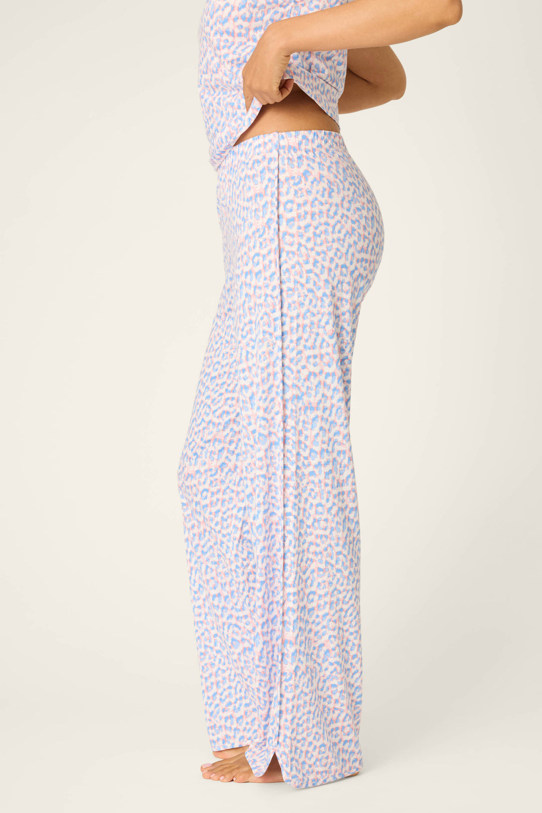 A person stands barefoot against a plain off-white background, wearing P.J. Salvage Animal Lover Leopard Print Open Leg Pants and a matching top. The waistband of the pants is visible as the top is lifted slightly.