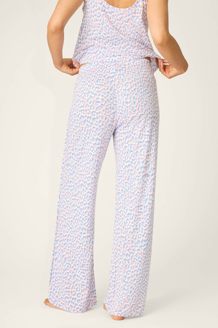 A person stands barefoot with their back to the camera, wearing P.J. Salvage’s Animal Lover Leopard Print Open Leg Pants in a light purple and pink leopard pattern, adjusting the waistband.