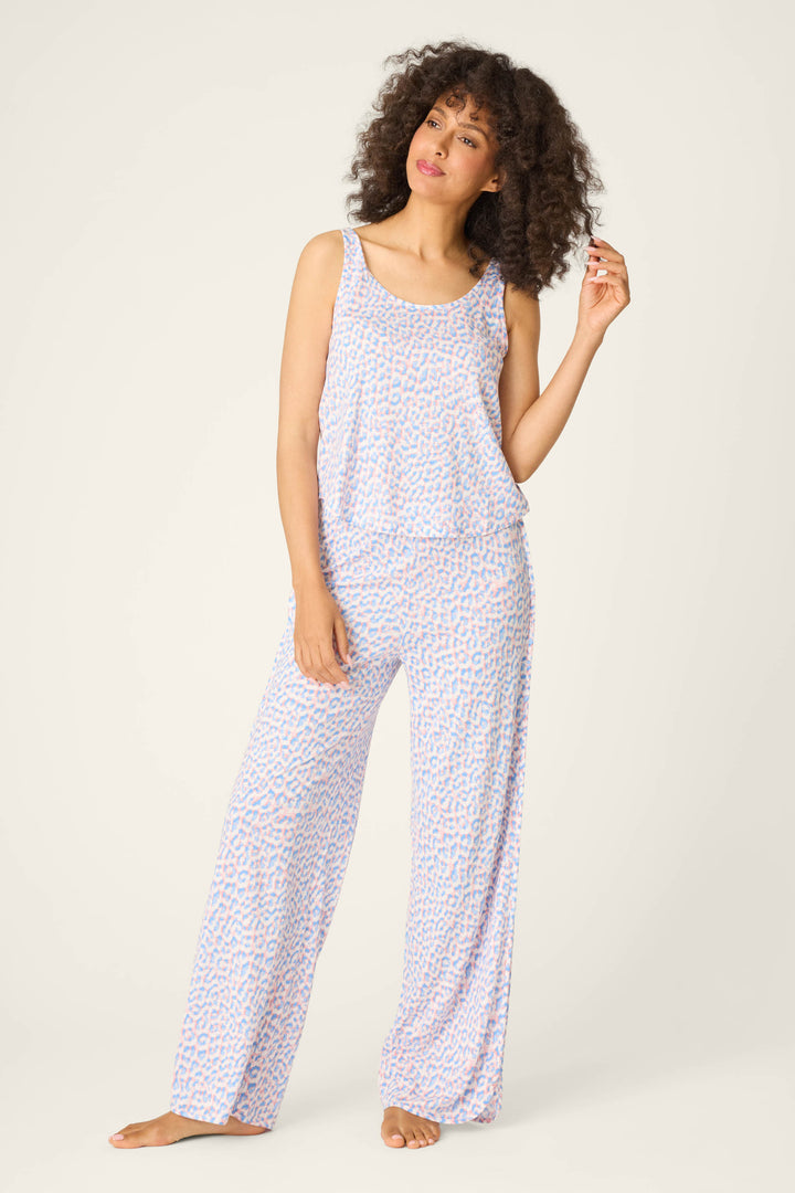 A woman stands barefoot against a plain background, wearing the P.J. Salvage Animal Lover Leopard Print Tank Top and matching wide-leg pants in a light blue and pink pattern, looking slightly to the side with one hand raised.