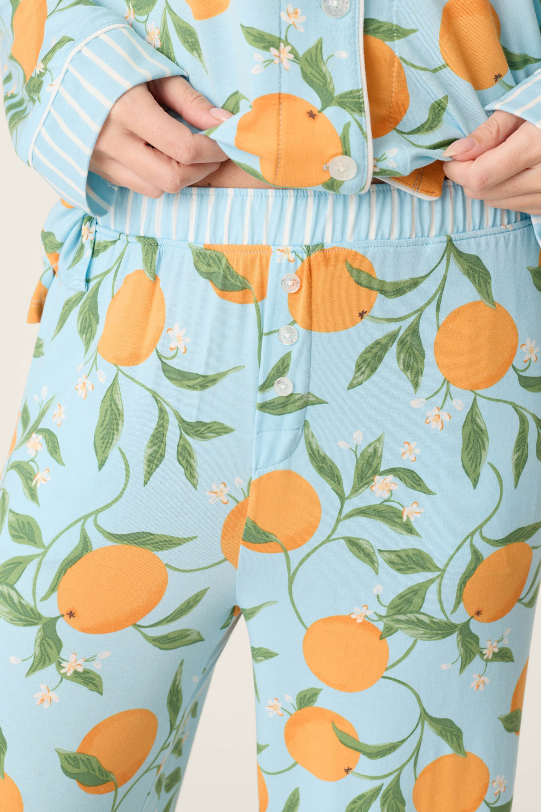 A person wears the Citrus Dreams Morning Squeeze Long 3-Piece PJ Set by P.J. Salvage, featuring a blue citrus print, buttoned shirt with white-striped sleeves, and matching elastic-waist pants with front white buttons.