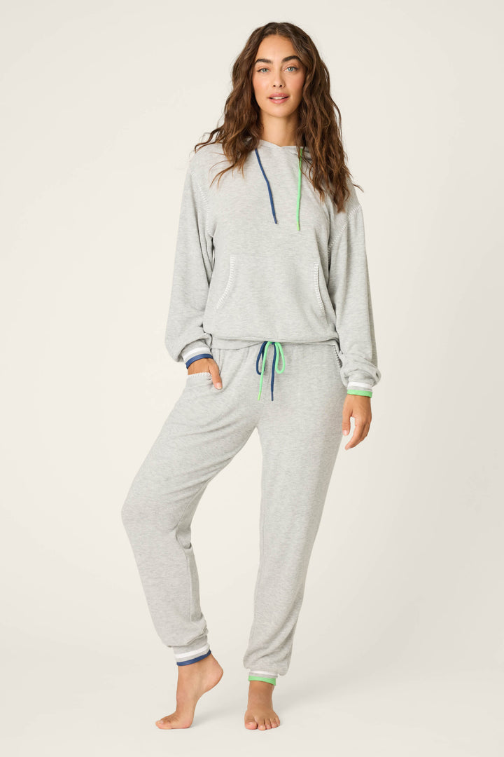 A woman stands barefoot against a plain background, wearing the P.J. Salvage C'est La Vie Heather Grey Hoodie with matching sweatpants, featuring blue and green drawstrings and cuffs, and has one hand in her pocket.