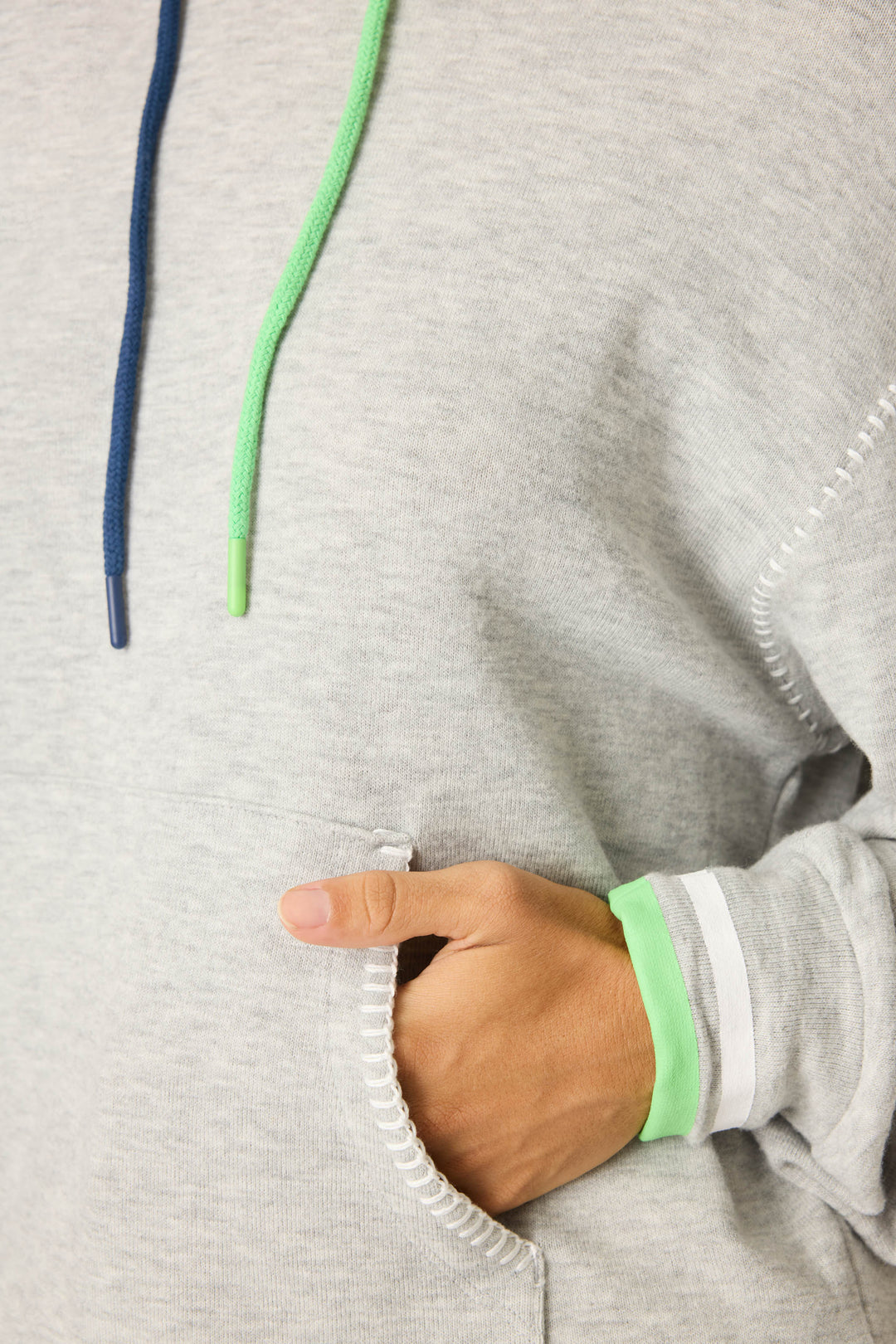 A person wearing the P.J. Salvage C'est La Vie Heather Grey Hoodie, featuring blue and green drawstrings, has one hand in the front pocket and a green wristband over the sleeve cuff.