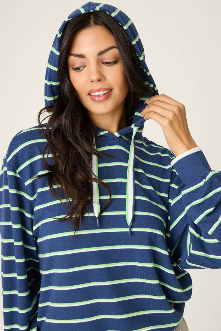 Wearing the P.J. Salvage C'est La Vie Striped Hoodie, a person holds a drawstring and looks down with a slight smile. The hoodie features blue, light green, and white horizontal stripes.