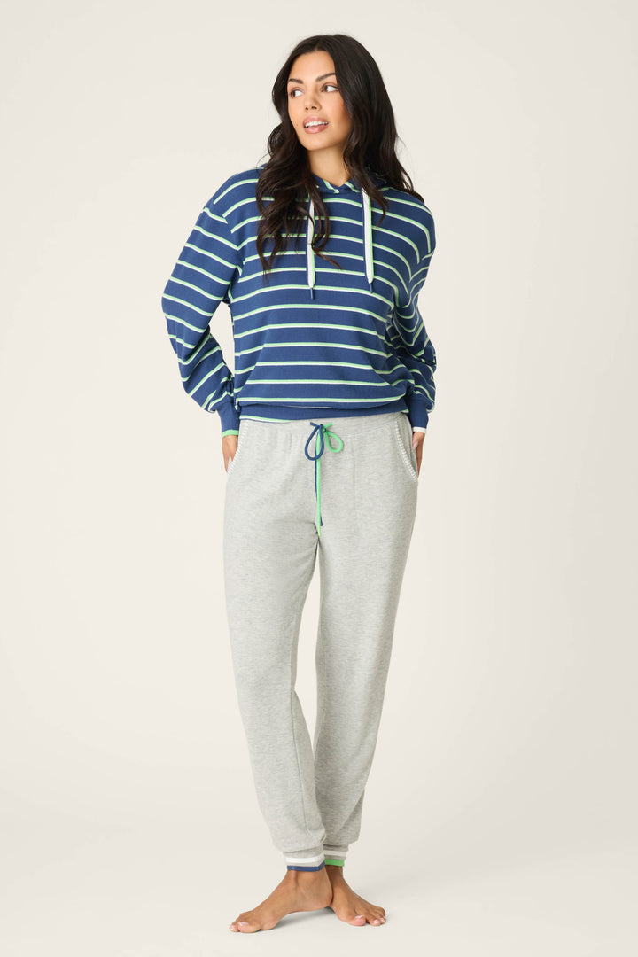 A person stands barefoot against a plain background, wearing the P.J. Salvage C'est La Vie Striped Hoodie with drawstring and light gray sweatpants, hands in pockets, looking to the side.