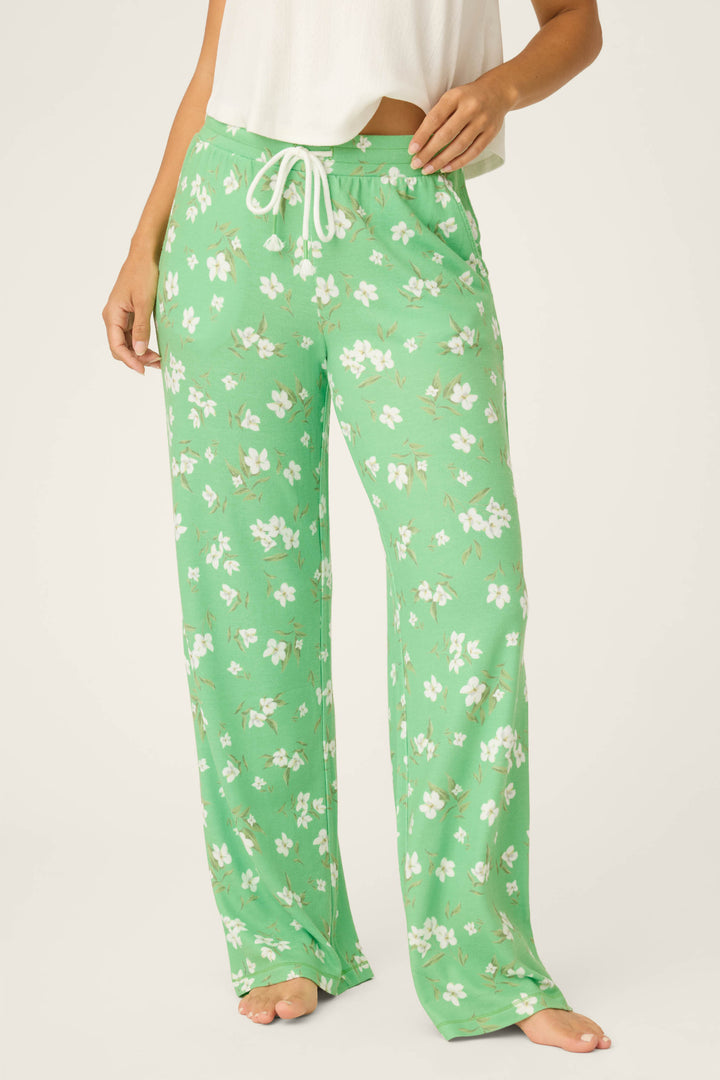 A person stands barefoot wearing P.J. Salvage C'est La Vie Floral Print Open Leg Pants, featuring a green and white floral pattern with a white drawstring, paired with a white cropped top. The image is cropped below the shoulders.