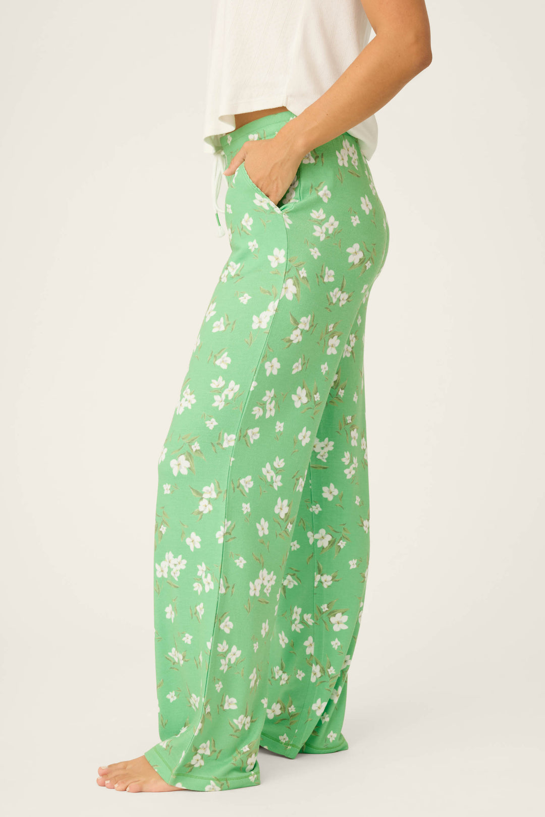 A person stands barefoot with one hand in the pocket, wearing P.J. Salvage C'est La Vie Floral Print Open Leg Pants in light green and a white short-sleeve top. The person's head is not visible.
