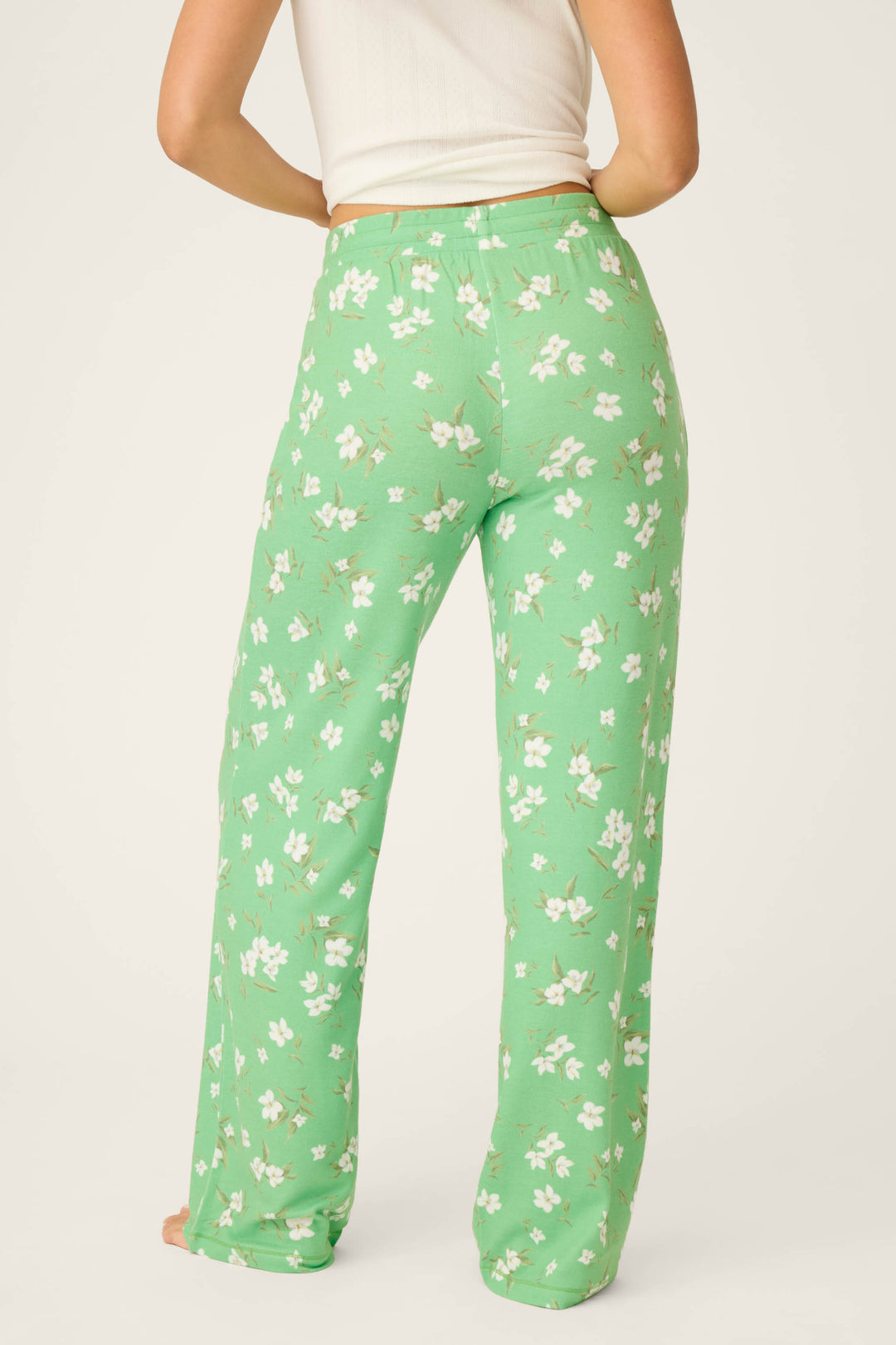 A person is shown from the back wearing P.J. Salvage C'est La Vie Floral Print Open Leg Pants, featuring a green color, loose fit, and small white floral patterns. Only the lower torso and legs are visible; styled with a white sleeveless top.