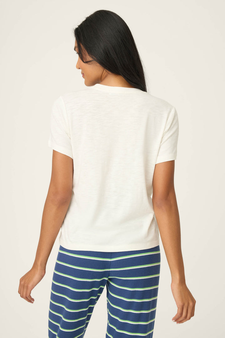 A person with long, dark hair is shown from the back, wearing the P.J. Salvage C'est La Vie Graphic Print Short Sleeve Top and blue pants with green and white horizontal stripes, standing against a neutral background.