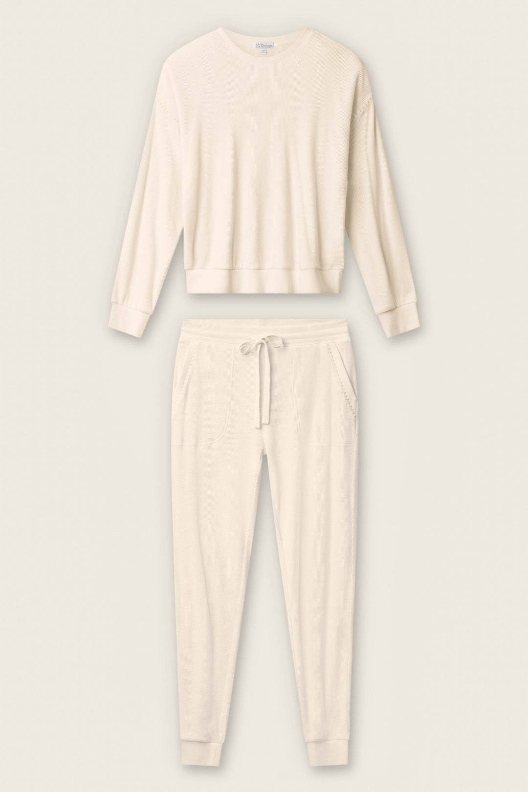 The P.J. Salvage Cross Stitch Casuals Light Beige Lounge Set features a long-sleeve crew neck top and drawstring jogger pants with pockets, shown laid flat on a neutral background.