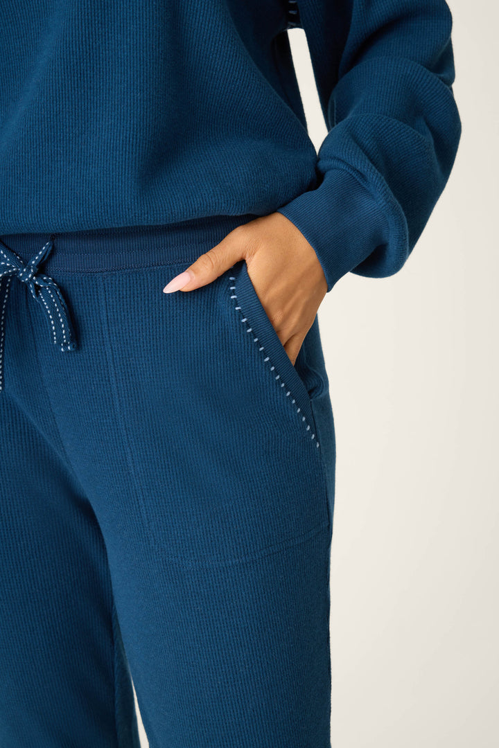 A person wears the P.J. Salvage Cross Stitch Casuals Navy Lounge Set, featuring visible stitching near the pocket and a patterned drawstring on the matching ribbed knit sweater and pants.