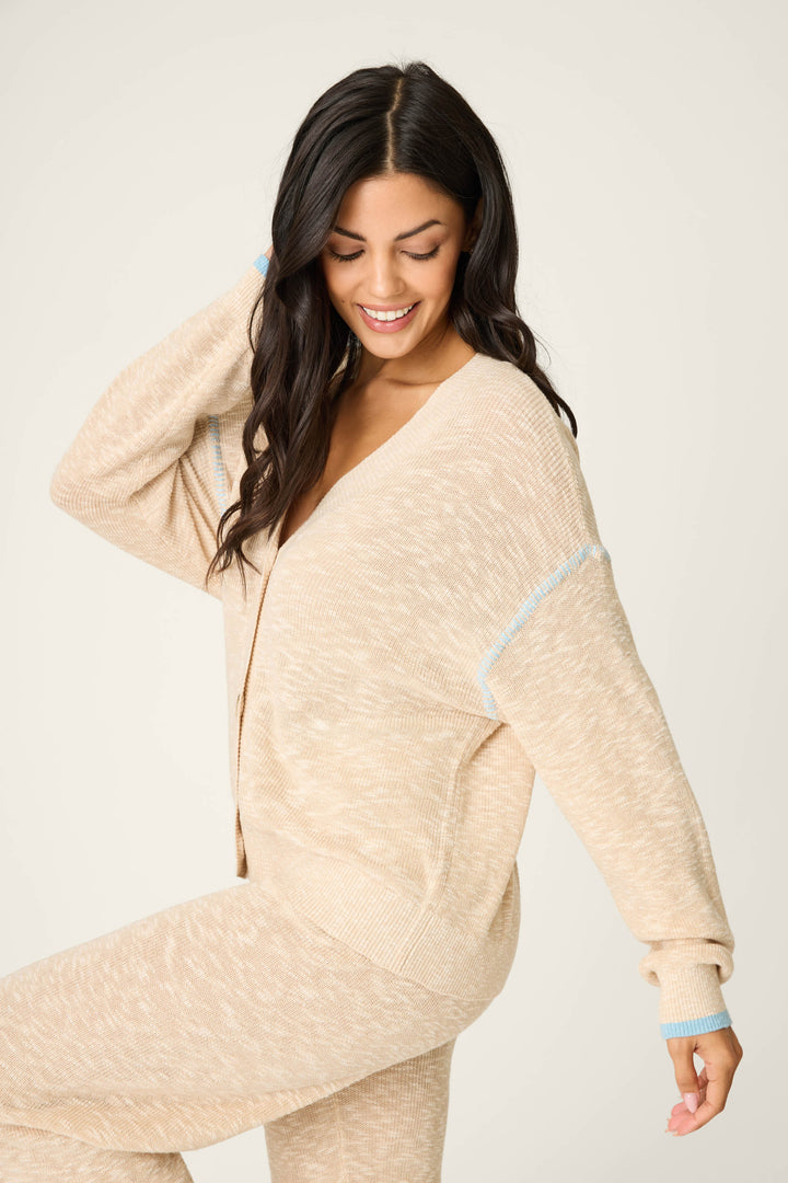 A woman with long dark hair smiles and looks down, wearing the P.J. Salvage Cozy Up Cotton Heather Sand Cardigan against a plain off-white background.