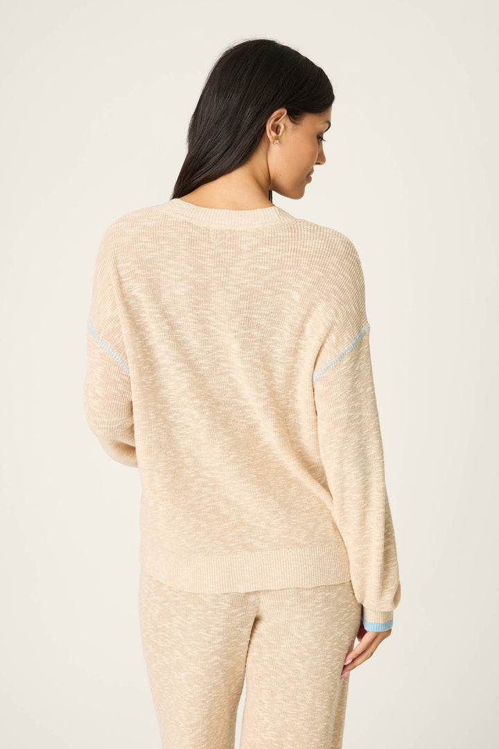 A woman with long dark hair is seen from the back wearing the P.J. Salvage Cozy Up Cotton Heather Sand Cardigan, a loose-fitting beige knit sweater, against a plain off-white background.
