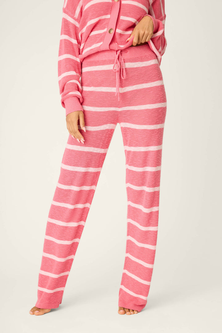 Wearing P.J. Salvage's Cozy Up Cotton Berry Kiss Open Leg Pants, a person stands barefoot against a plain light background. The pink and white striped knit pants are paired with a matching long-sleeve top; the face is not visible.