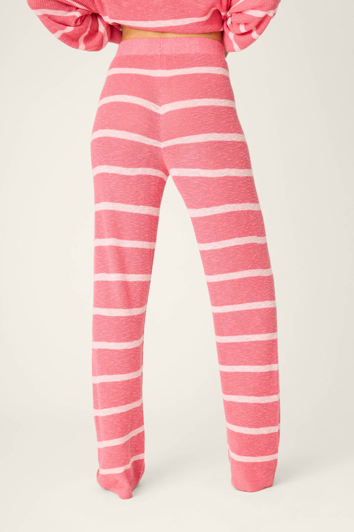 A person faces away from the camera wearing P.J. Salvage Cozy Up Cotton Berry Kiss Open Leg Pants, featuring a high waist, pink knit fabric with horizontal white stripes, a loose fit, and paired with a matching pink top.