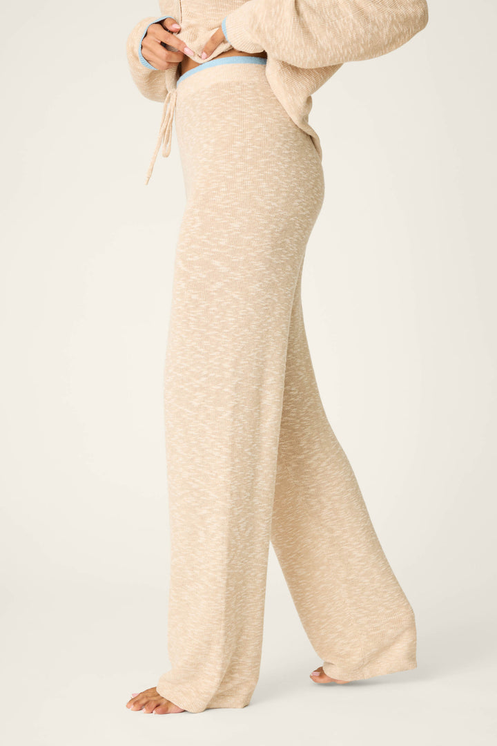 A person stands barefoot in P.J. Salvage Cozy Up Cotton Heather Sand Open Leg Pants, shown from the side, shoulders to feet, with hands adjusting the high-waisted waistband.