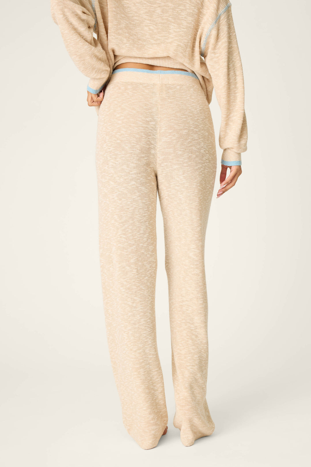 A person is shown from the back wearing P.J. Salvage’s Cozy Up Cotton Heather Sand Open Leg Pants, which are high-waisted with a relaxed fit. The pants are beige and loose-fitting, and the background is plain and light-colored.