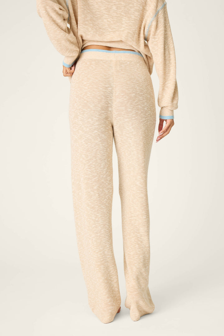 A person is shown from the back wearing P.J. Salvage’s Cozy Up Cotton Heather Sand Open Leg Pants, which are high-waisted with a relaxed fit. The pants are beige and loose-fitting, and the background is plain and light-colored.