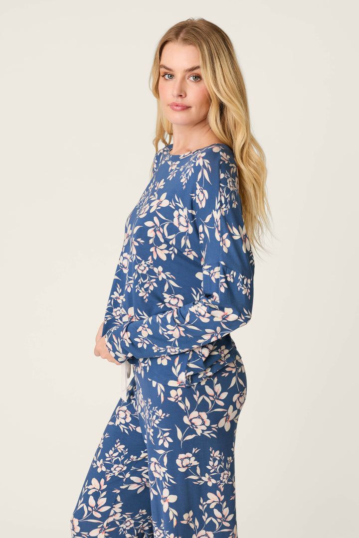A woman with long blonde hair models the P.J. Salvage Flora Dreams Twilight Garden Long Sleeve PJ Top, paired with matching pants, as she poses sideways and looks at the camera against a plain light background.