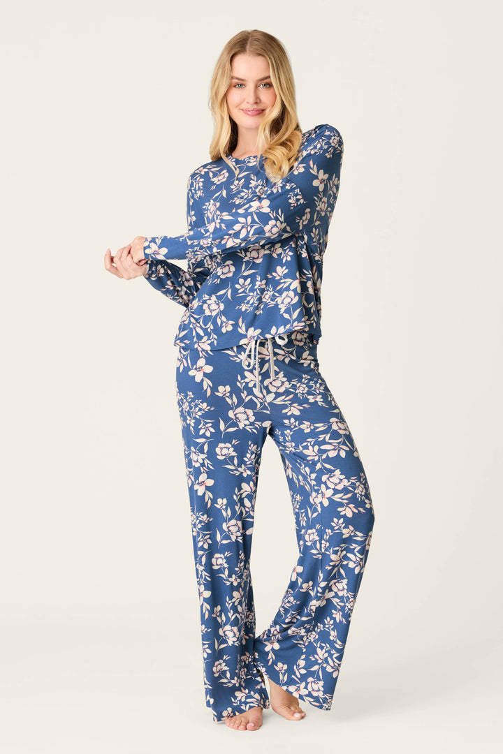 A woman smiles barefoot in the P.J. Salvage Flora Dreams Twilight Garden Long Sleeve PJ Top, showcasing its relaxed fit and blue modal jersey with a white floral pattern as she holds out one side of the top.