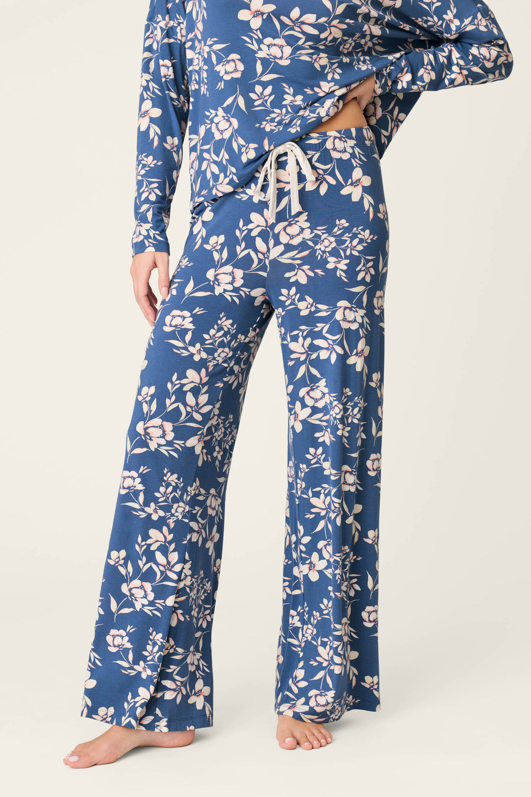 A person stands barefoot against a plain background, wearing P.J. Salvage Flora Dreams Twilight Garden Open Leg PJ Pants—a matching blue floral set in soft modal jersey with long sleeves and wide-leg, drawstring waist lounge pants.