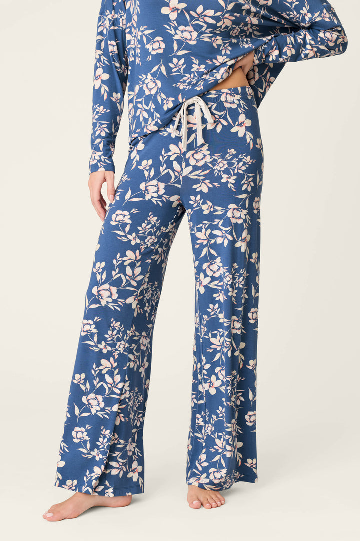 A person stands barefoot against a plain background, wearing P.J. Salvage Flora Dreams Twilight Garden Open Leg PJ Pants—a matching blue floral set in soft modal jersey with long sleeves and wide-leg, drawstring waist lounge pants.