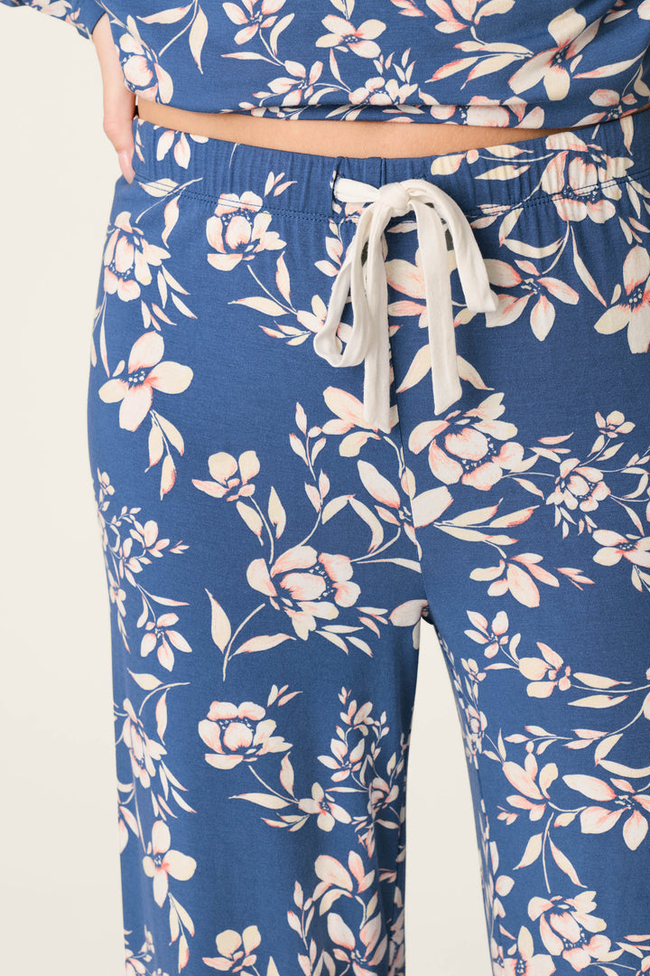 A close-up of the lower torso and upper legs shows a person wearing P.J. Salvage Flora Dreams Twilight Garden Open Leg PJ Pants in blue floral modal jersey with a white drawstring, paired with a matching top.