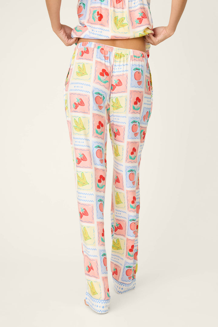 A person is shown from the back wearing P.J. Salvage Frutta Fresca Summer Harvest Open Leg Pants with a colorful fruit-print pattern; the matching top is partly visible against a plain, light background.
