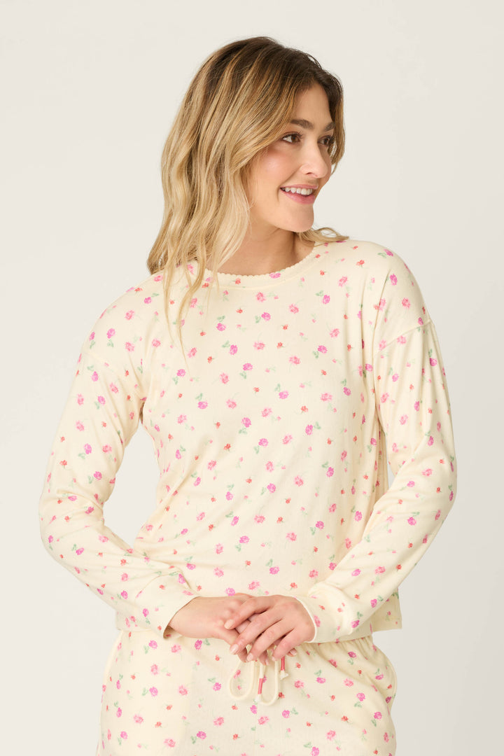 A person wears the For the Mamas Butter Blooms Long Sleeve Top by P.J. Salvage, featuring a butter yellow base and pink floral pattern, standing with hands clasped and smiling against a plain background.