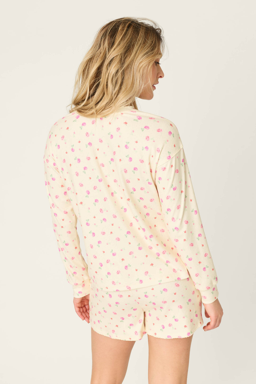 A person with blonde hair is shown from the back in a P.J. Salvage For the Mamas Butter Blooms Long Sleeve Top, a butter yellow pointelle pajama top with a small pink floral print. The background is plain and light-colored.