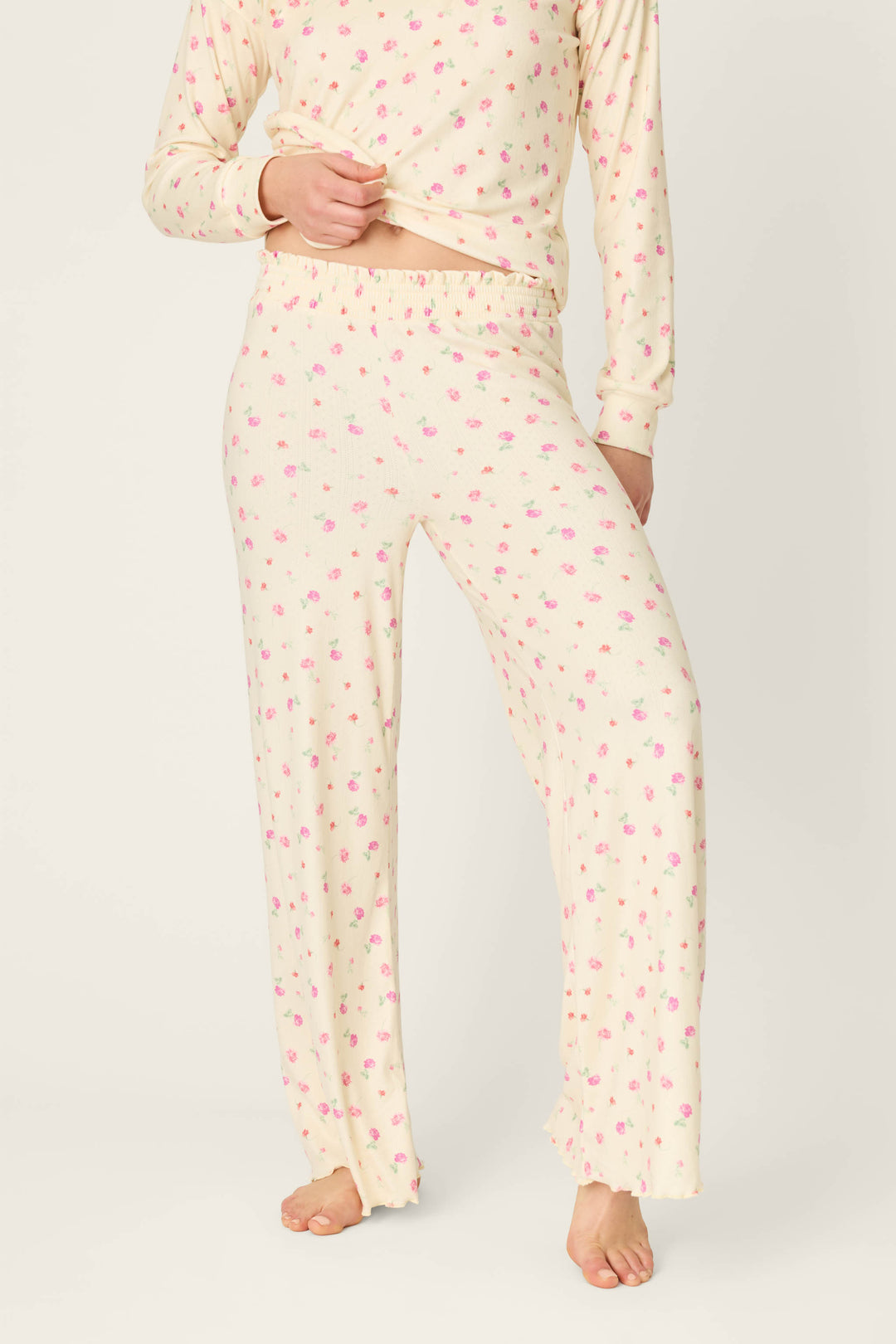 A person stands barefoot against a plain background, wearing P.J. Salvage's For the Mamas Butter Blooms Open Leg Pajama Pants in cream with a pink floral pattern and a matching long-sleeve top, with their face not shown.