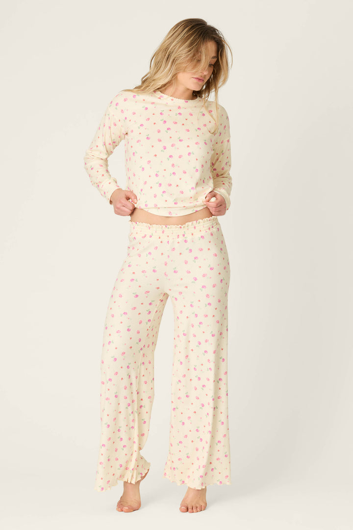 A person stands barefoot against a plain light background, wearing P.J. Salvage's For the Mamas Butter Blooms Open Leg Pajama Pants in cream with a pink floral pattern and matching long-sleeve top.