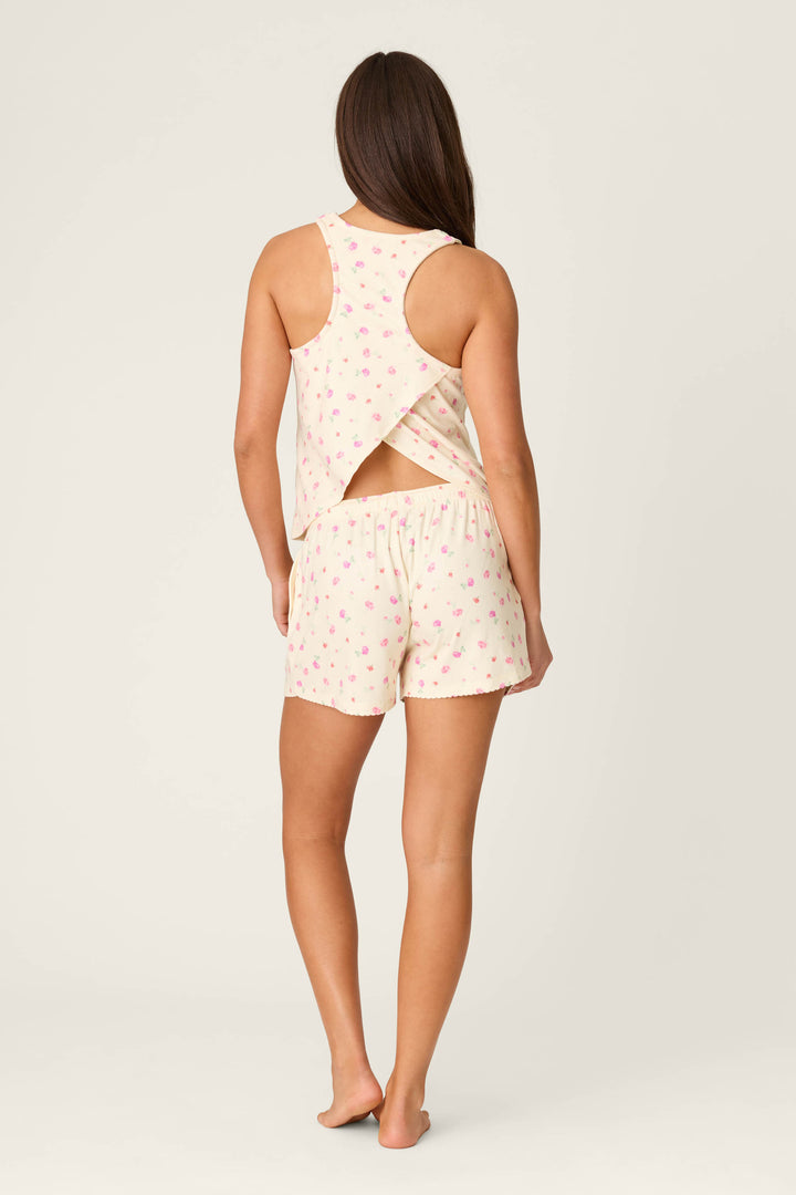A person stands barefoot, wearing the P.J. Salvage For the Mamas Butter Blooms Short PJ Set—cream with a pink floral print. The tank top has a crisscross back and an open section above the waist, paired with matching shorts.
