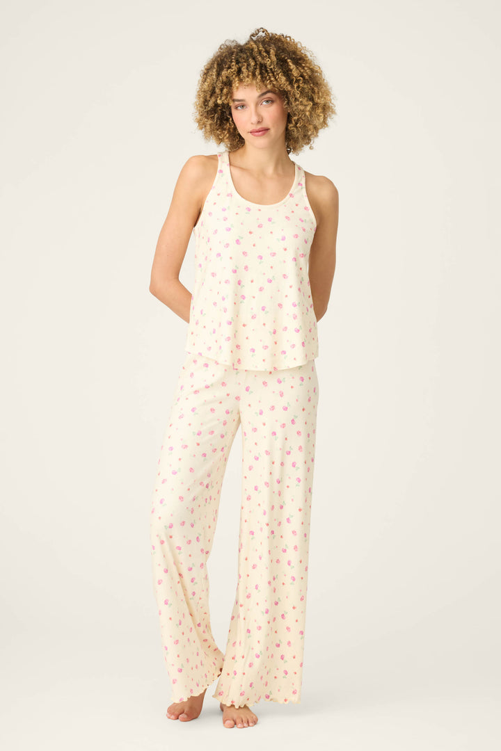 A person stands barefoot against a plain background, wearing the P.J. Salvage For the Mamas Butter Blooms Long PJ Set—a butter yellow sleeveless top and wide-leg pants with a small pink floral pattern.