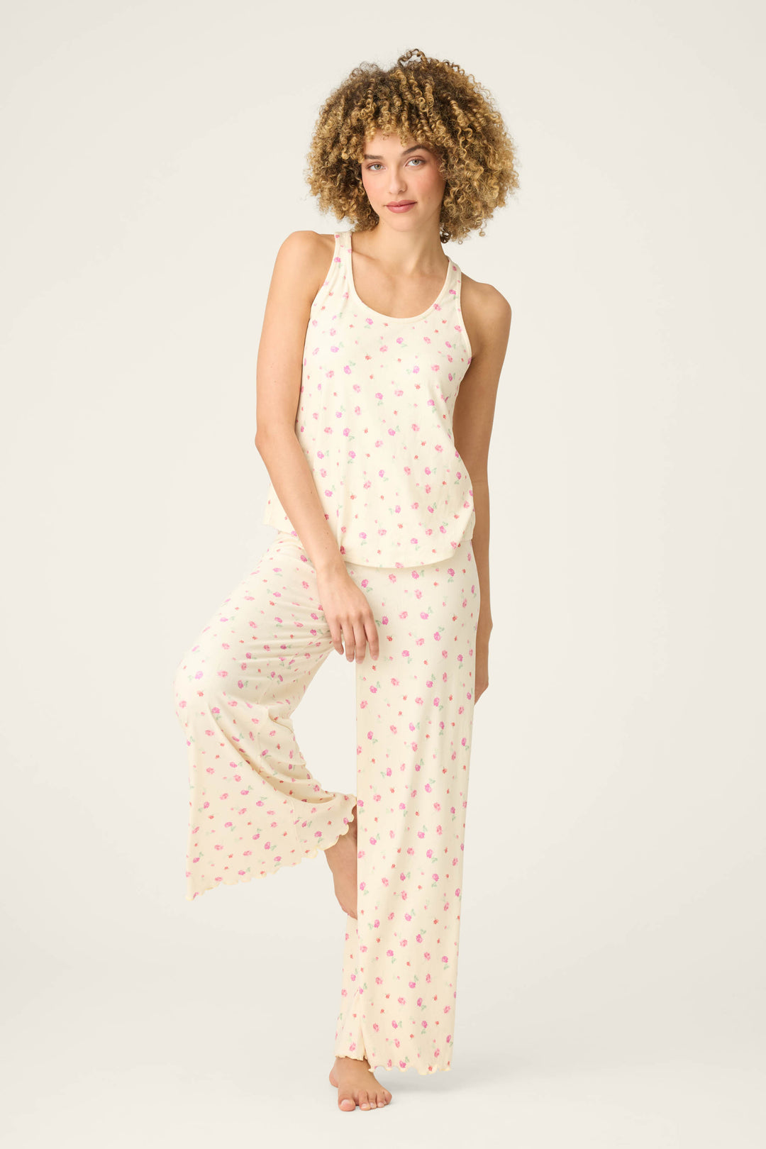A person with curly hair stands barefoot on one leg, wearing a matching cream pajama set and the P.J. Salvage For the Mamas Butter Blooms Tank Top, against a plain light background.