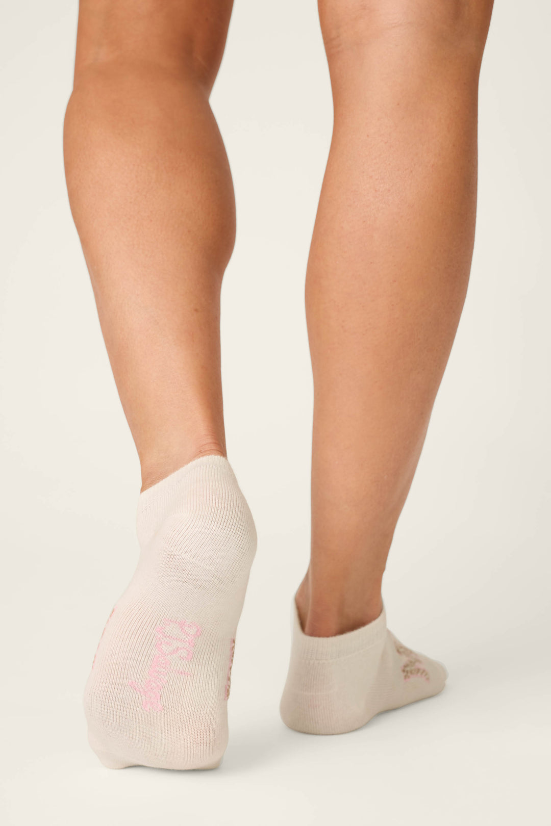 A person is standing on a light surface, wearing cream ankle socks with subtle pink soles from the Luxe Leopard Dreams 3-Pack Ankle Socks by P.J. Salvage—perfect for cozy, French-inspired lounging at home.