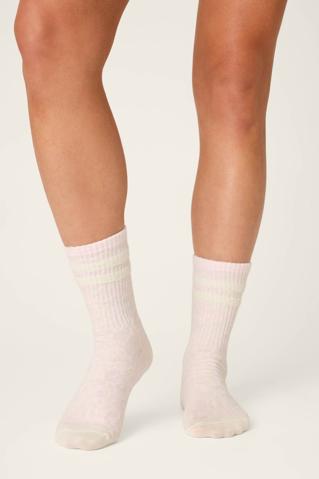 A person wearing P.J. Salvage Luxe Leopard Dreams Ribbed Crew Socks in ballet-pink stands on an off-white background, with only their lower legs and feet visible.