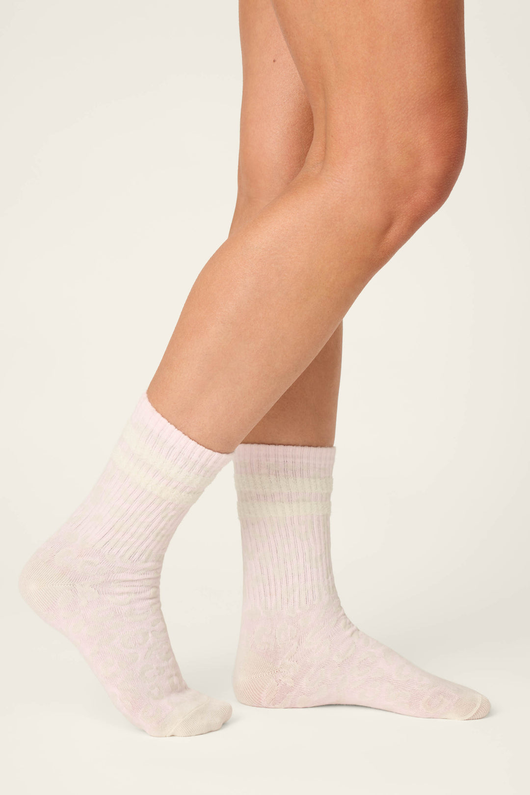 A person wears P.J. Salvage Luxe Leopard Dreams Ribbed Crew Socks in ballet-pink, showing only their lower legs and feet against a plain white background.